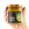 Hand holding a jar of Siam Green Thai Curry Paste with a white background