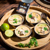 Four bowls of Tom Kha soup on a wooden tray with limes and a box of Siam Tom Kha.