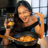 Woman holding a wok of pad thai and a package of SIAM brand pad thai noodles kit.
