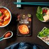 Siam Thai Soup Tom Yum package on a dark surface with ingredients and soup.